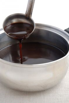 sauce being poured into a pan on a white tablecloth with a spoon in it