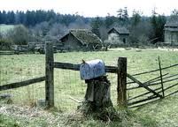 a mailbox in the middle of a field near a wooden fence and some houses