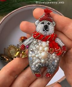 a person holding a teddy bear brooch with pearls and beads on it's chest