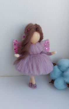 there is a small doll next to two balls of yarn on the floor and one has a purple dress