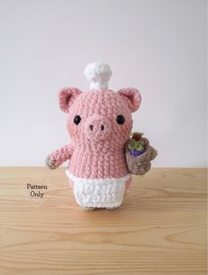 a crocheted pig holding a small plant in it's hand on top of a wooden table