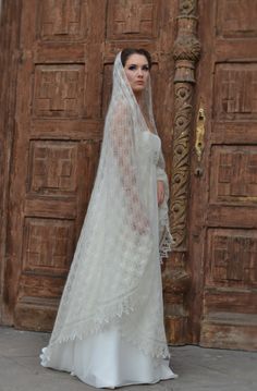 a woman in a white wedding dress standing next to a wooden door wearing a veil