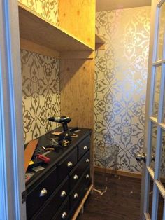 an empty closet with drawers and shelves in the corner, next to a wallpapered wall