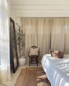 a bedroom with a bed, chair and rugs in front of a window that has sheer curtains