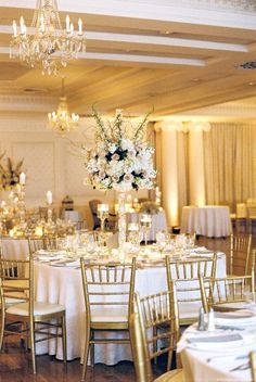 a room filled with tables and chairs covered in white table cloths next to a chandelier