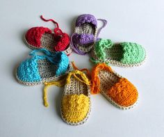 six crocheted baby shoes are arranged in a circle on a white table top