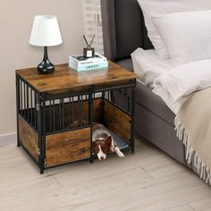 a dog in a crate under a bed next to a night stand with a lamp on it