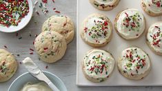 cookies with white frosting and sprinkles are on a plate next to a bowl of whipped cream