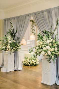 flowers are in white vases with drapes on the windowsill and curtains behind them