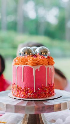 a pink cake with white icing and sprinkles on top sitting on a table