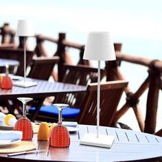 an outdoor dining area with tables and chairs overlooking the ocean in front of a wooden fence