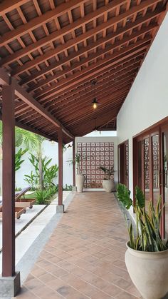 an outdoor covered patio area with potted plants and wooden beams on the ceiling, surrounded by brick pavers