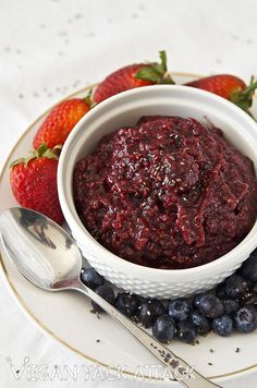 a white bowl filled with blueberries and strawberries on top of a plate next to two spoons