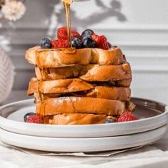 a stack of french toast with berries and syrup being drizzled on top