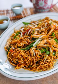 a white plate topped with noodles and vegetables next to a cup of tea on a table