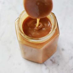 a jar filled with peanut butter on top of a white counter next to a spoon