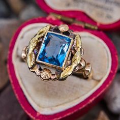 This lovely vintage ring features a lab created blue spinel in a full bezel setting that is decorated with a foliate motif halo. The ring is crafted in patinated 10k yellow gold and is currently a size 6.5. Blue Art Deco Jewelry Stamped 14k, Antique Blue Rings With Rose Cut Diamonds, Vintage Gold Ring With Halo Setting, Antique Sapphire Ring With Halo Setting, Heirloom Topaz Ring With Rose Cut Diamonds, Collectible Vintage Sapphire Ring, Victorian Blue Rings With Rose Cut Diamonds, Vintage 14k Gold Sapphire Gemstone Ring, Vintage Yellow Gold Sapphire Ring