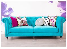 a blue couch with colorful pillows on it in front of a purple flowered wall