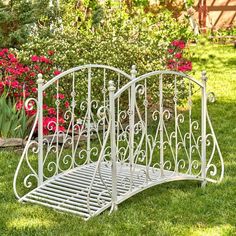 a white metal bed frame sitting on top of a green grass covered field next to flowers