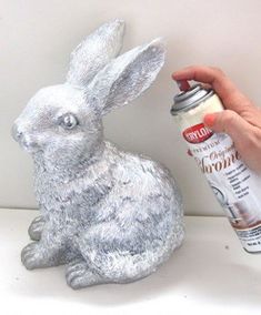 a person is spray painting a rabbit statue with silver paint on it's body