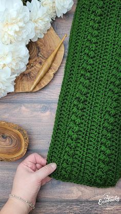 someone is holding the edge of a green crocheted blanket on a wooden table