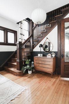 a room with a wooden floor and stairs next to a mirror on the wall near a dresser