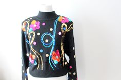 a black sweater with multicolored flowers and swirls on the front, sitting on a mannequin