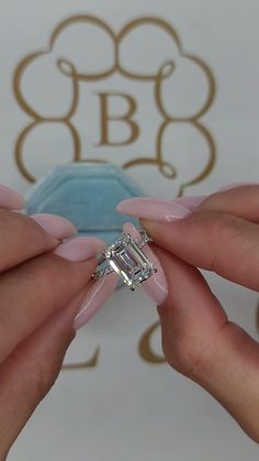 two hands holding an engagement ring in front of a wall with the initials b & g on it