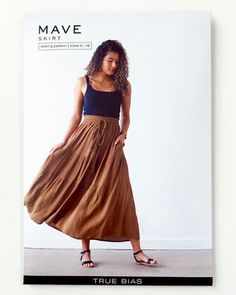 a woman wearing a skirt and sandals standing in front of a white wall with the words mave on it