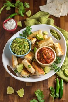 a white plate topped with tacos and guacamole next to lime wedges