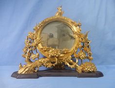 an ornately decorated gold mirror on top of a wooden stand with blue background and white backdrop