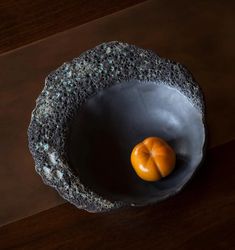 an orange sitting in a black bowl on top of a wooden table