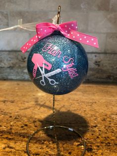 a blue ornament with pink ribbon and scissors on it sitting on a stand