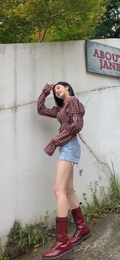 a woman standing in front of a wall with her hands on her head and wearing red boots