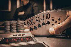 two hands holding playing cards on top of a table