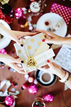 two hands holding a white gift box on top of a table with pink and gold confetti