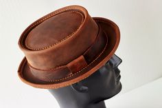 Introducing our handmade, genuine leather hat in a beautiful shade of brown.  The Classic Pork Pie style gives this hat a timeless, elegant look.  Crafted from high-quality leather, this hat is not only stylish but also durable and long-lasting.  Each hat is made by hand, ensuring that every piece is unique and of the highest quality. Perfect for both casual and formal occasions, this hat is a versatile addition to any wardrobe.  Its classic design is sure to never go out of style and it's a mus Fitted Leather Hat With Curved Brim, Classic Leather Top Hat With Short Brim, Fitted Leather Hat With Short Brim, Classic Short Brim Leather Top Hat, Rustic Leather Brimmed Hats, Fitted Leather Top Hat With Short Brim, Fitted Leather Top Hat With Flat Brim, Distressed Brown Leather Brimmed Hat, Vintage Brown Leather Brimmed Hat