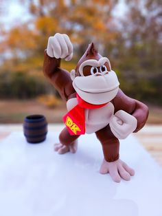 a monkey figurine is posed on top of a white surface with trees in the background