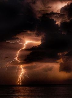 a large cloud filled with lots of lightning in the night sky over water and land