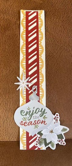 a close up of a paper christmas ornament on a brown surface with white and red ribbon