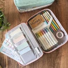 an open suitcase filled with lots of different colored pens and pencils on top of a wooden table