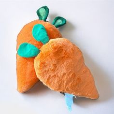 an orange stuffed animal with green leaves on it's head and tail sitting on a white surface