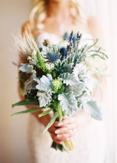 a woman holding a bouquet of flowers and greenery in front of a white wall