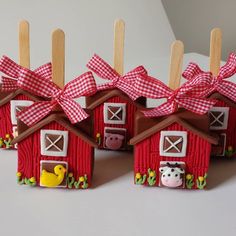 three small red houses with farm animals on them, tied to wooden clothes pegs