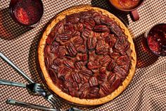 a pecan pie on a checkered table cloth next to two cups and spoons