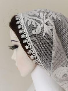 a white mannequin headpiece with lace on it's sides and an intricately designed veil