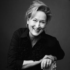 a black and white photo of a woman sitting on a chair smiling at the camera