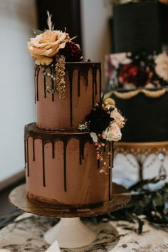 two tiered chocolate cake with flowers on the top and bottom, sitting on a table