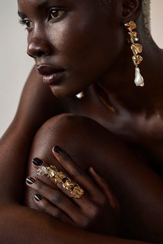 a woman with dark skin and gold jewelry on her arm, posing for the camera