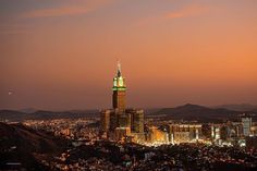 the city lights are green and white in the night sky as seen from atop a hill